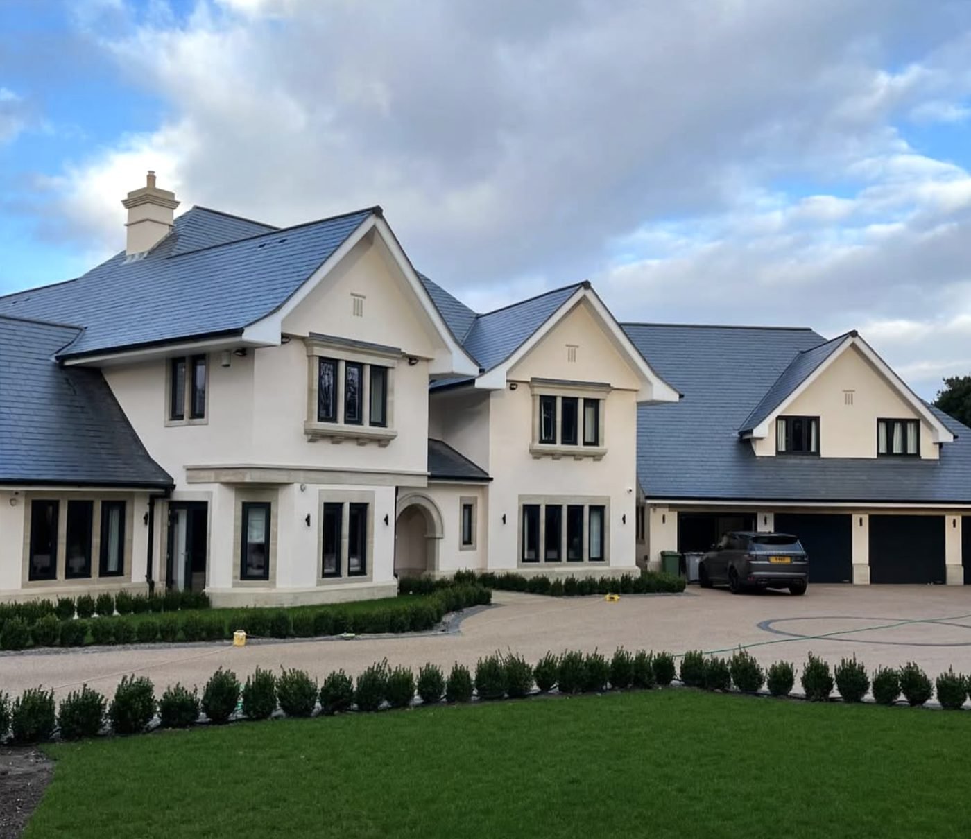 Large detached house finished in a pale through-coloured render with dressed stone surrounds